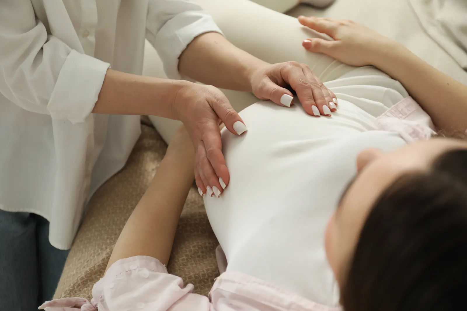 Ventre de femme enceinte entouré de mains, dans des draps clairs